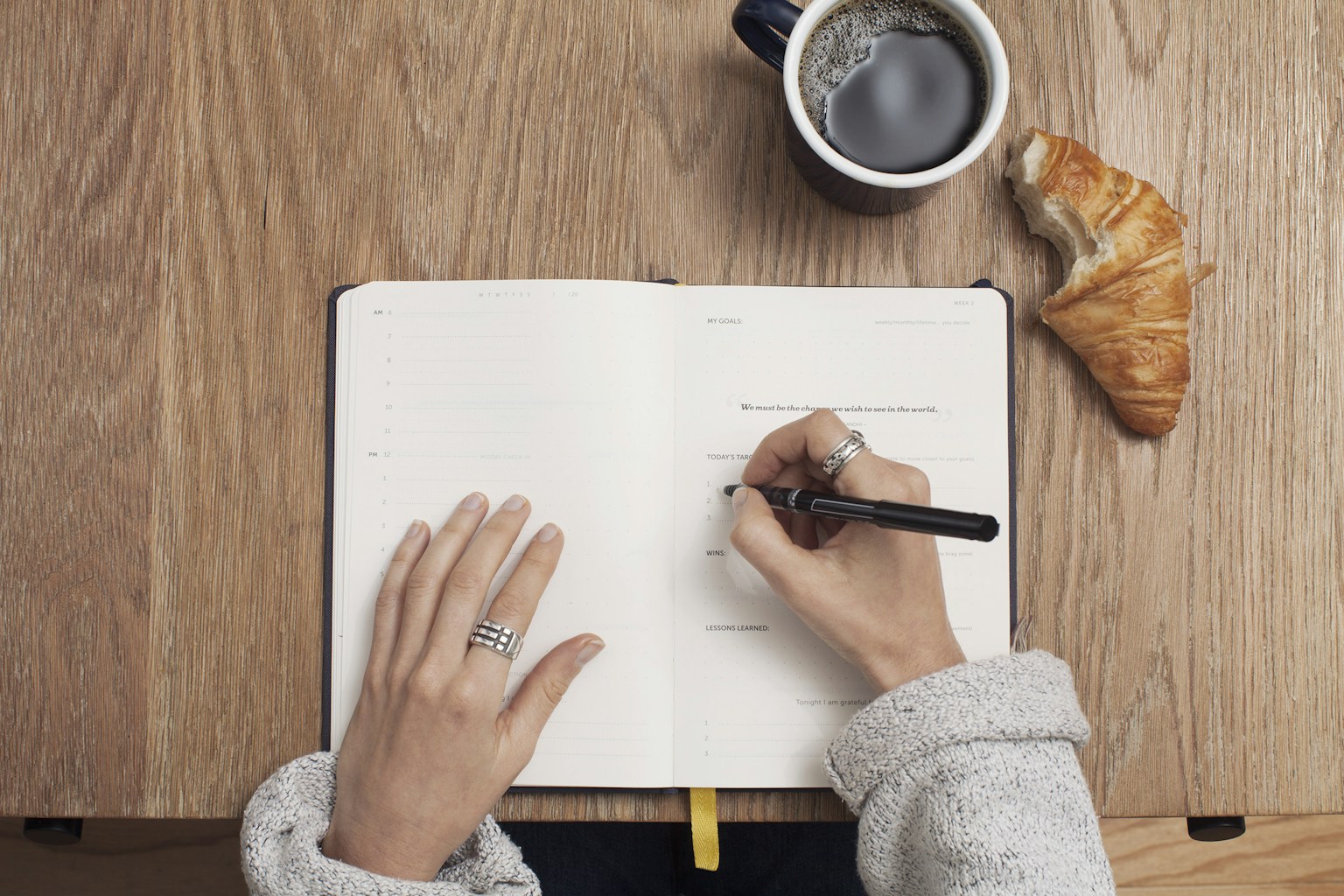 Person writing a daily entry in an open notebook at a wooden desk